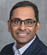 A man wearing a suit and tie smiles for the camera. Description generated by AI