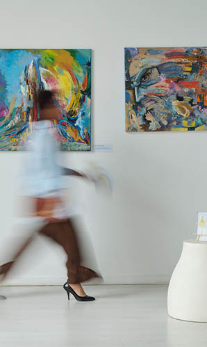 A woman in a blue shirt is walking in front of a wall of paintings. Description generated by AI
