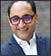 A man wearing a blue suit and a white shirt with purple glasses. Description generated by AI