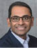 A man wearing a blue suit and glasses. Description generated by AI
